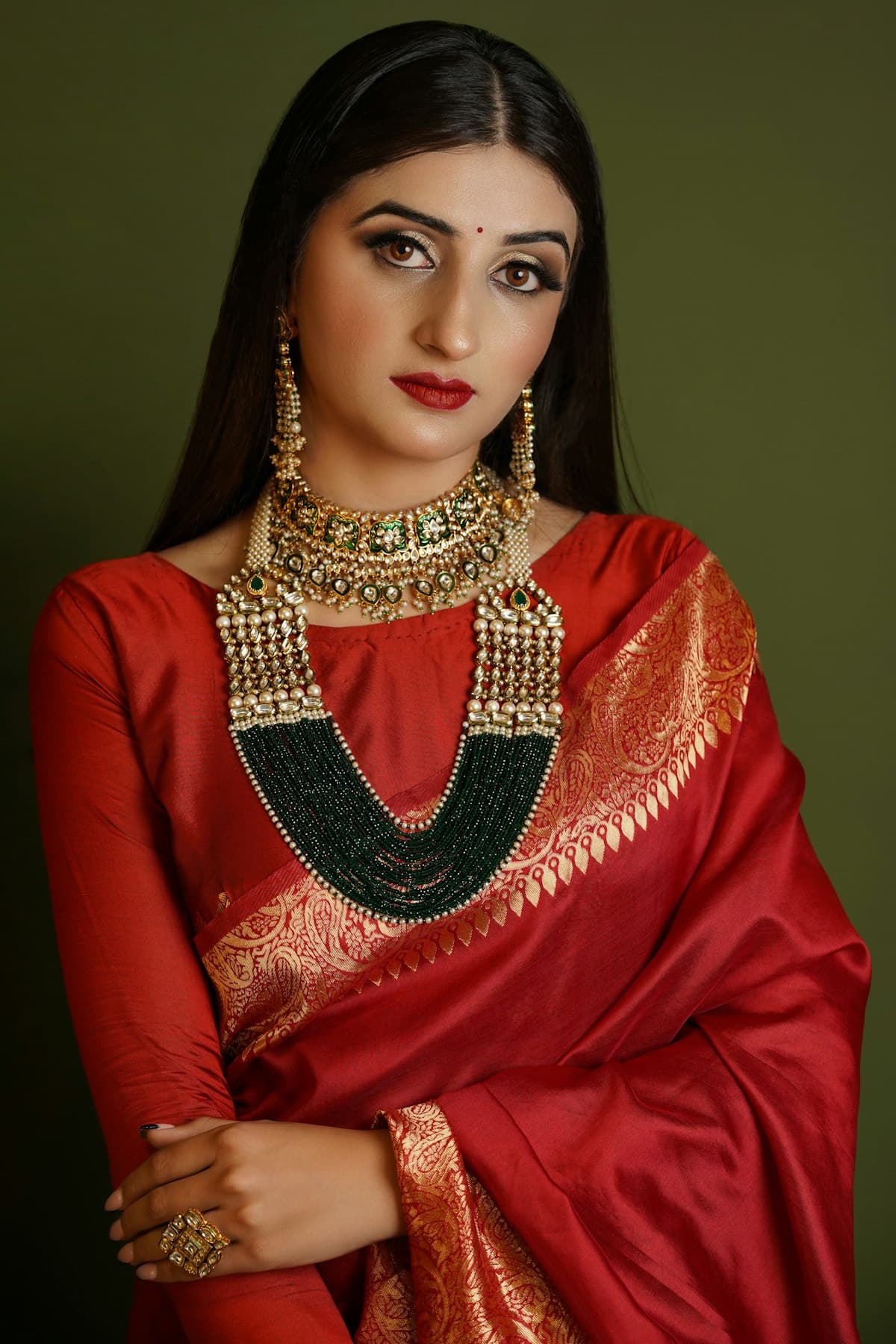 An editorial portrait of a model in a red saree and gold jewellery