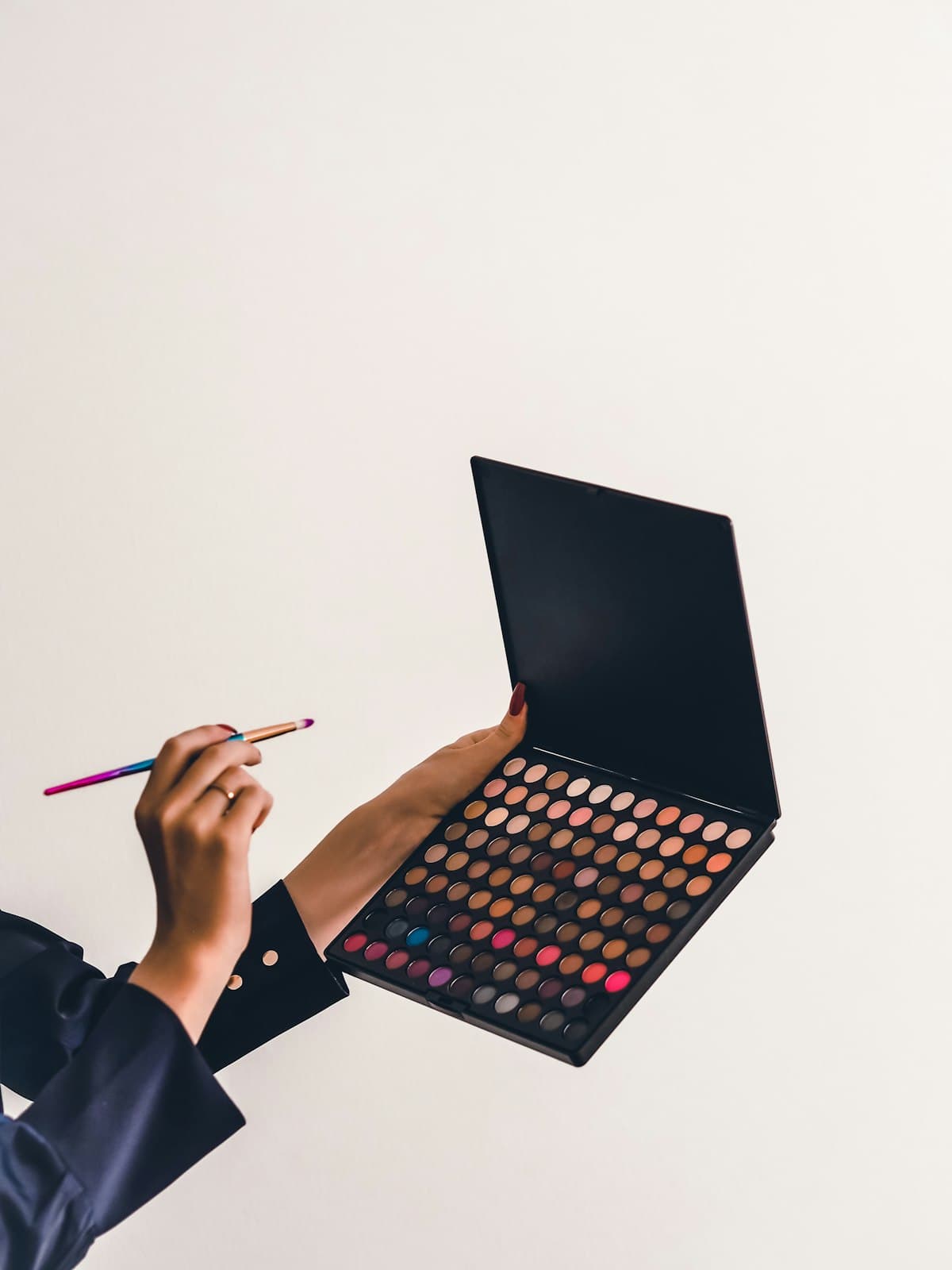 Hands holding an eyeshadow palette and brush